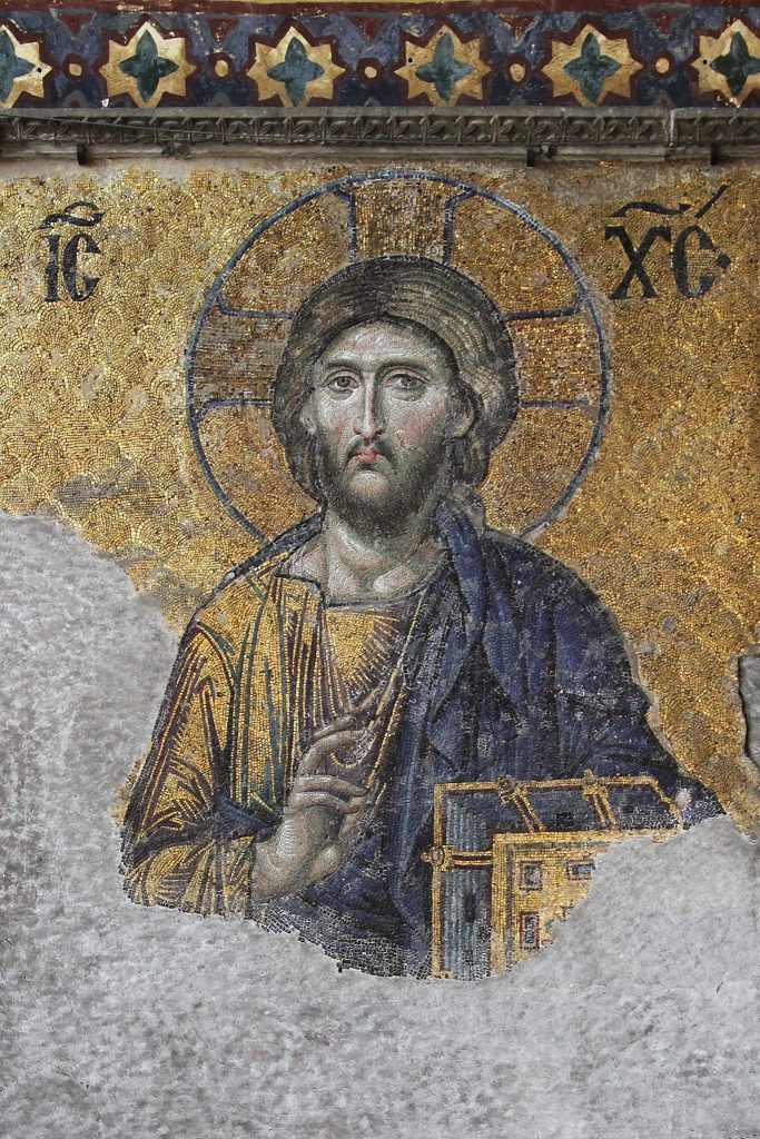 Image of Jesus found within the Hagia Sophia. Carrying a gold-covered New Testament, Jesus looks forward at the onlooker giving a gesture of blessing with his left hand. On either side of the icon are both halves of the Greek Christogram which together spell Jesus Christ.